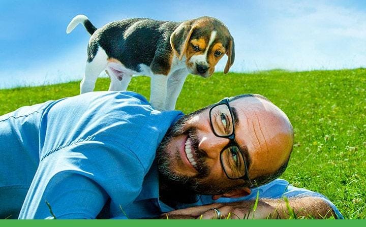 man lying in a field of grass with his puppy