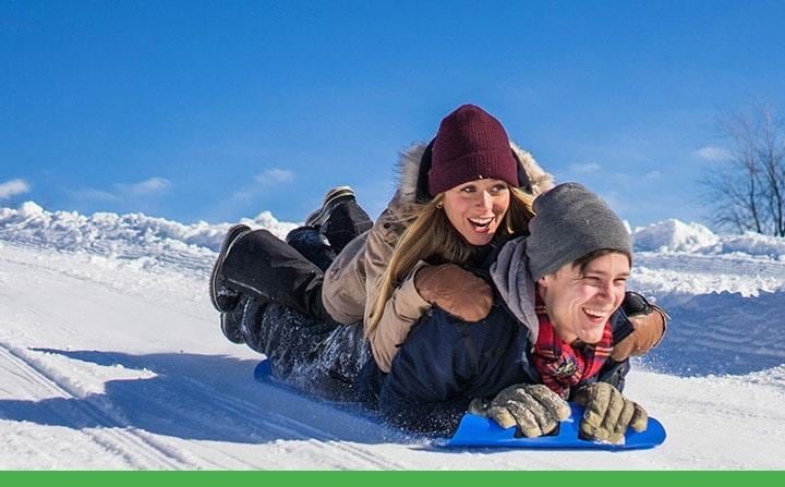 Young couple sledding down a snowy hill together